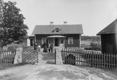 1 man 2 kvinnor och 2 barn framför liten träbyggnad
