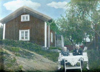 Man och kvinna sittande vid trädgårdsmöbel framför byggnad
