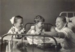 Pojke i säng omgiven av 2 sjuksköterskor
