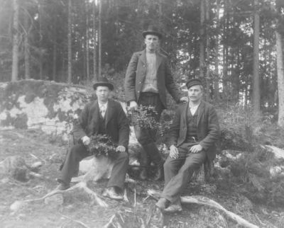 2 sittande och 1 stående man i skogen
Nyckelord: Dräkt
