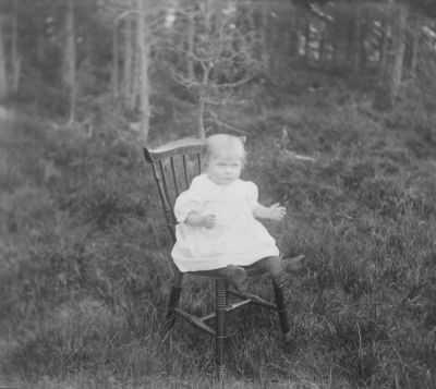 Liten flicka sittande på pinnstol i skogen
