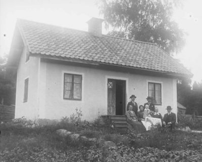 3 kvinnor 3 män och 1 flicka framför hus på landet
Nyckelord: Dräkt Gärdesgård