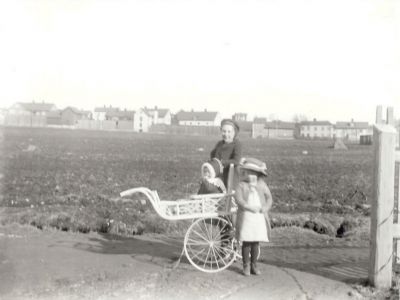 3 barn och barnkärra med stadsbebyggelse i bakgrunden
Nyckelord: Barnvagn Dräkt