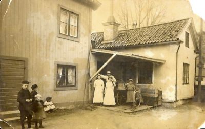 2 kvinnor 1 man och 5 barn framför byggnad
Nyckelord: Dräkt Kärra