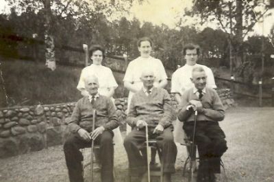 3 äldre män sittande utomhus med 3 vårdare stående bakom
Nyckelord: Käpp 