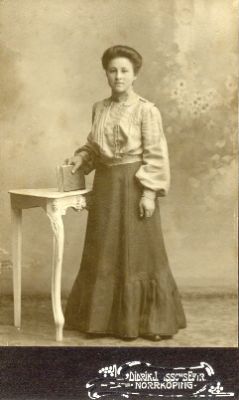 Kvinna stående vid bord med bok i handen
Maja Göthberg
Nyckelord: Dräkt