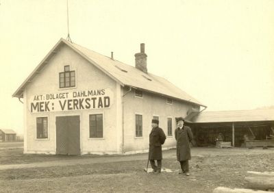 2 män framför verkstadsbyggnad
