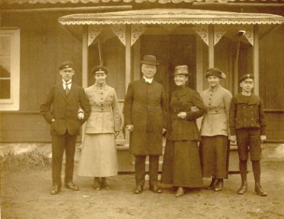 Familj framför byggnad
Nyckelord: Dräkt Hatt Skolmössa