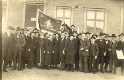 En gruppmänniskor stående med standar framför byggnad
