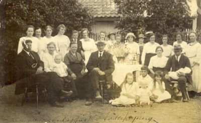 En grupp festklädda personer sittande i trädgård
