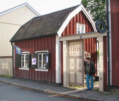 Litet rött trähus med fönsterluckor
