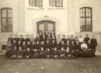 Elever och lärare framför skolbyggnad
