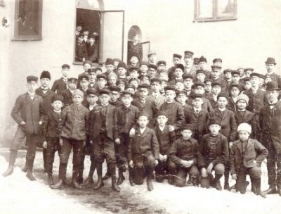Skolpojkar med lärare framför skola
