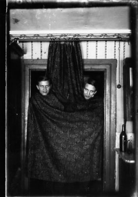 2 män stående insvepta i ett draperi i dörröppning.
Nyckelord: Frisör Draperi