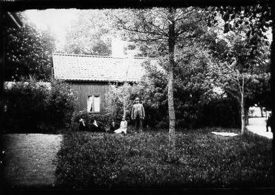 3 män och 1 kvinna sittande och man stående framför byggnad.
