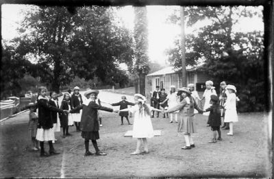 Barn dansande ringdans kring midsommarstång.
