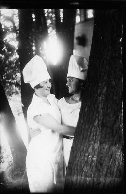 2 kvinnor stående intill träd.
Nyckelord: Kockmössa