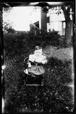 Flicka sittande i barnstol på gräsmatta.
Nyckelord: Barnstol