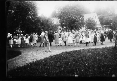Ett antal personer dansande ringdans i park.
Nyckelord: Ringdans