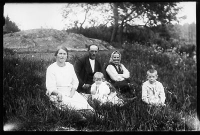 Man, 2 kvinnor, pojke och flicka sittande i gräset.
