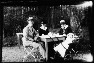 Man, 2 kvinnor sittande vid kaffebord i naturen. Barn sittande i vagn.
Nyckelord: Serveringsmöbler Barnvagn