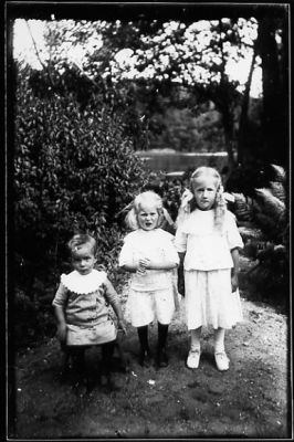 3 barn stående i trädgård.
