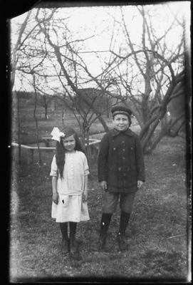 Pojke och flicka stående i trädgård.
