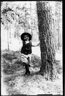 Barn stående vid träd i skogsbacke.
