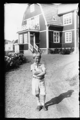 Pojke stående på grusgång framför byggnad.
Nyckelord: Grusgång