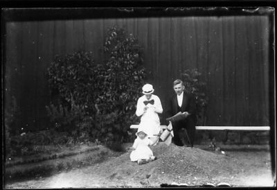 Man och kvinna sittande på bänk och flicka sittande i sandhög.
