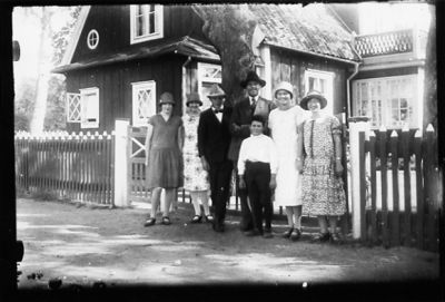2 män, 4 kvinnor och 1 pojke stående framför byggnad.
Keywords: Prästgård Staket