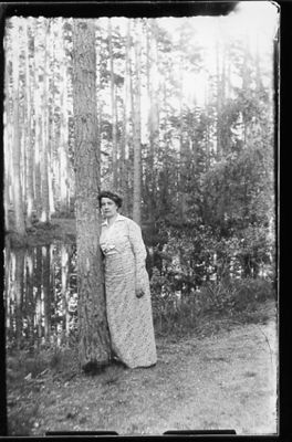 Kvinna stående vid träd med tjärn i bakgrunden.
Nyckelord: Tjärn