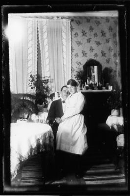 Man sittande i stol med kvinna i knät, i rum.
Nyckelord: Spegel Duk Gardin