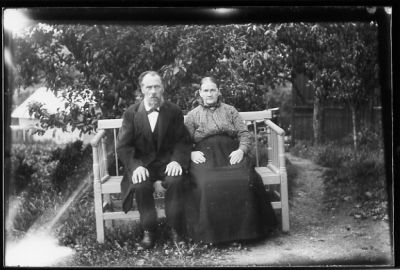 Man och kvinna sittande på bänk i trädgård.
Nyckelord: Bänk