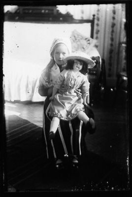 Flicka sitter med docka i knät.
