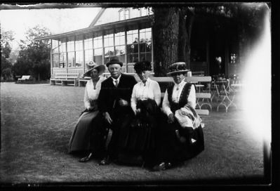 Man och 3 kvinnor sittande på bänk framför byggnad.
