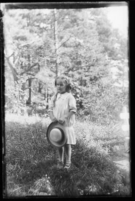 Flicka stående i skogsbacke.
Nyckelord: Hatt