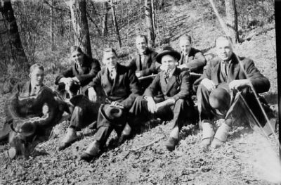 7 män sittande i skogsbacke.
Nyckelord: Skogsbacke Pipa