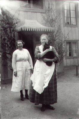 2 kvinnor stående framför byggnad. Den ena med en katt i famnen.
Nyckelord: Katt Bostad