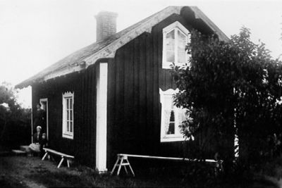 1 kvinna stående, 1 sittande och ett barn sittande på trappa till byggnad.
Nyckelord: Bänk
