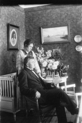 Man sittande och kvinna stående i rum.
Nyckelord: Tapet Tavla Blommor