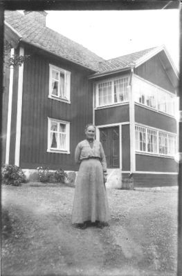 Kvinna stående på gårdsplan med byggnad i bakgrunden.
