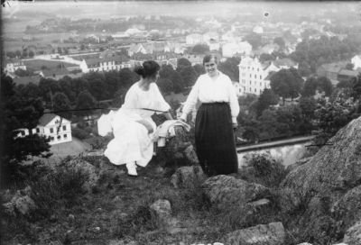 Kvinna stående och kvinna sittande på berg med stadsvy i bakgrunden.
Nyckelord: Utsikt