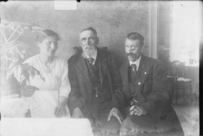 2 män och kvinna sittande vid bord i rum.
