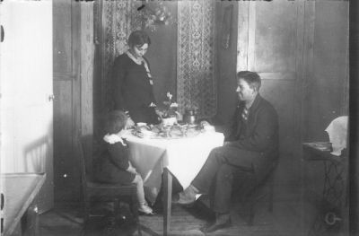 Man och flicka sittande och kvinna stående vid bord i rum.
Nyckelord: Kaffe