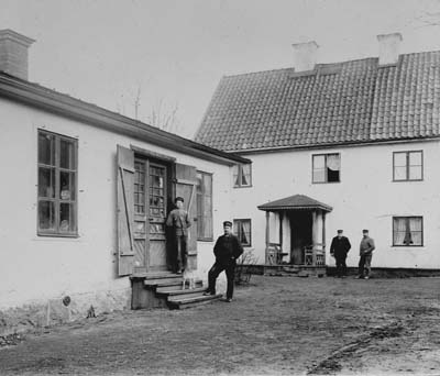 4 män stående på gårdsplan framför byggnader
