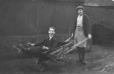 En man skjutsande en annan man på skottkärra
Nyckelord: Skottkärra
