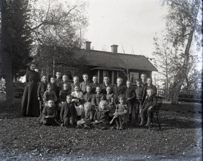 Kvinna och en grupp barn framför byggnad
Nyckelord: Skola