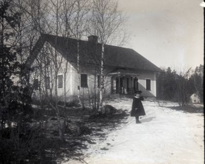 Flicka på snöig väg framför hus
