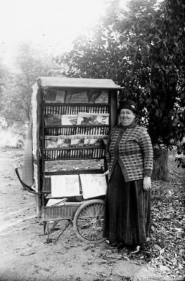 Kvinna stående framför ambulerande tidningsvagn.
Nyckelord: Tidningsvagn